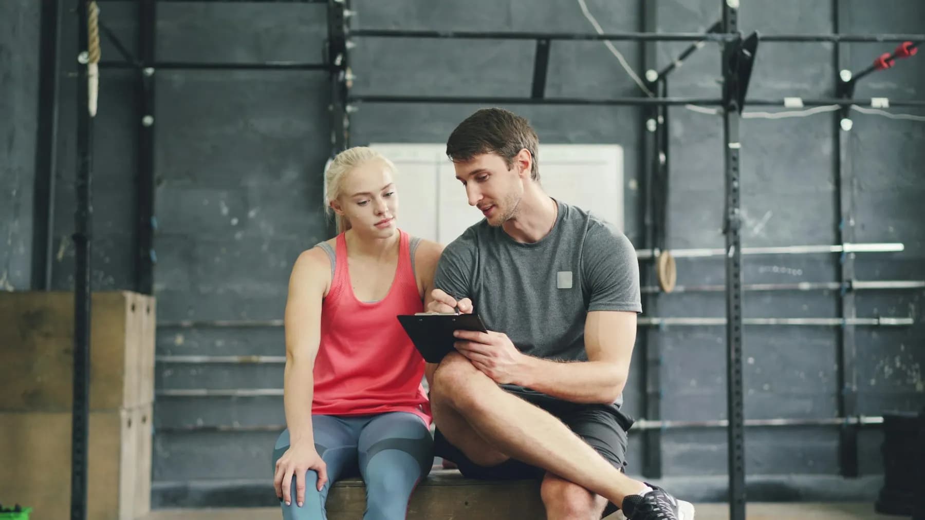 Um treinador revê um plano de treino numa prancheta com uma cliente no ginásio